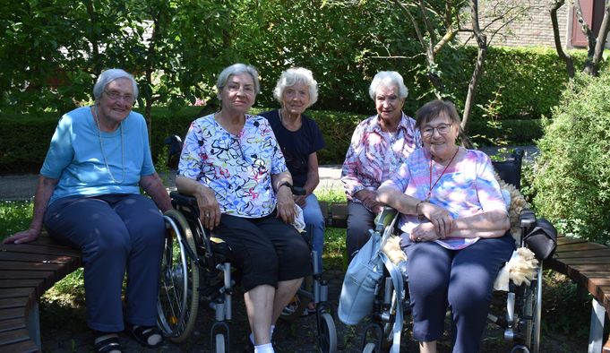 Fünf ältere Frauen im Garten, zwei sitzen im Rollstuhl